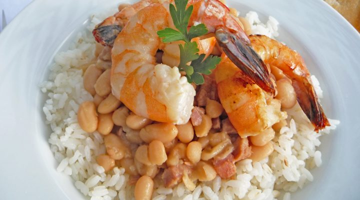 a close up of a plate of new orleans style white beans with a shrimp on top