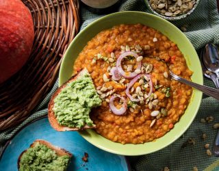 bowl of yellow split pea butternut squash stew with purple onions and a side of bread with a green dip on it