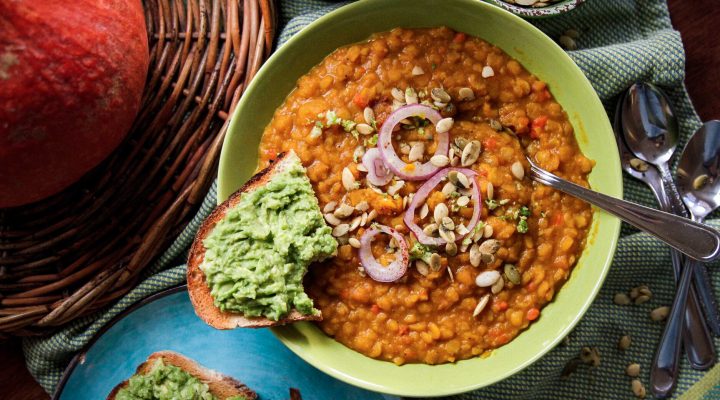 bowl of yellow split pea butternut squash stew with purple onions and a side of bread with a green dip on it