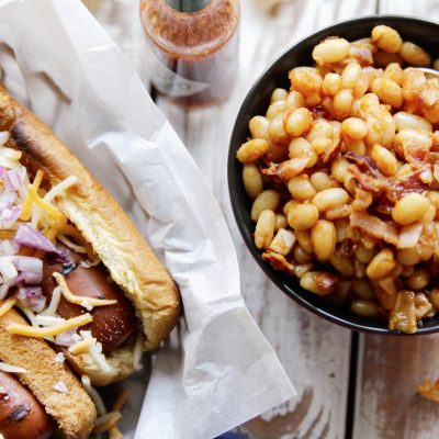 Chipotle Baked Beans in a bowl next to 2 grilled hot dogs