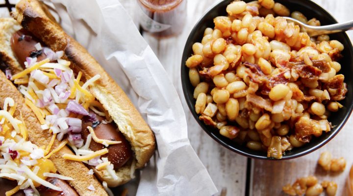 Chipotle Baked Beans in a bowl next to 2 grilled hot dogs