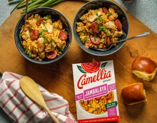 Gluten Free Cajun Jambalaya in 2 smal bowls next to a box of camellia brand cajun seasoning mix and 2 small bread rolls