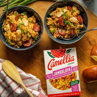 Gluten Free Cajun Jambalaya in 2 smal bowls next to a box of camellia brand cajun seasoning mix and 2 small bread rolls