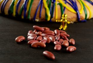 a king cake baby next to a king cake by a pile of red beans