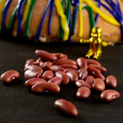 a king cake baby next to a king cake by a pile of red beans