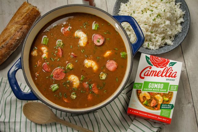 Stovetop Cajun Gumbo in a blue dutch oven featuring shrimp and sasuage next to a box of camellia brand gumbo roux base and a plate of white rice