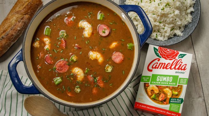 Stovetop Cajun Gumbo in a blue dutch oven featuring shrimp and sasuage next to a box of camellia brand gumbo roux base and a plate of white rice