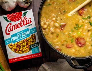 Stovetop Cajun White Beans in a dutch oven next to a box of cajun white bean seasoning