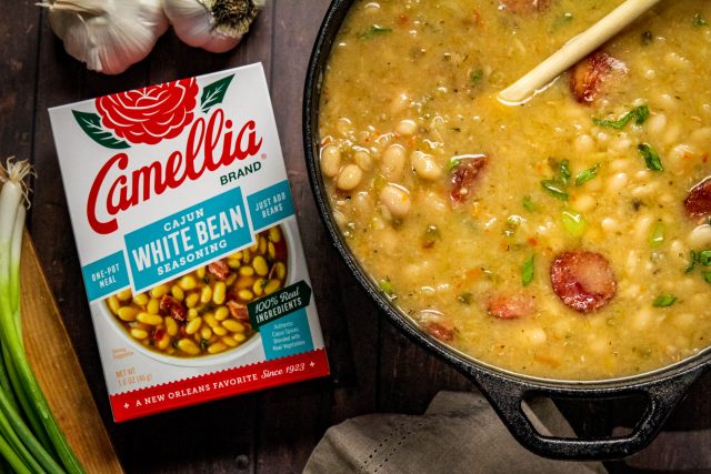 Stovetop Cajun White Beans in a dutch oven next to a box of cajun white bean seasoning