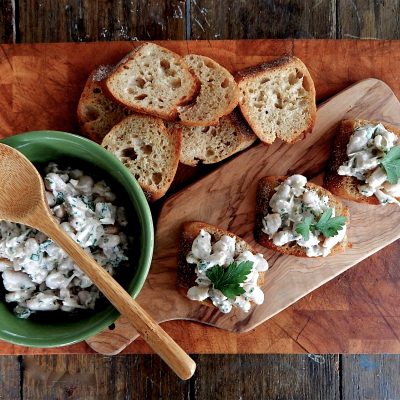 a bowl of Caesar-Style White Beans next to small pieces of bread with the beans on it