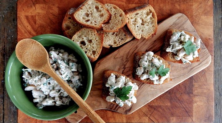 a bowl of Caesar-Style White Beans next to small pieces of bread with the beans on it