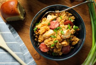 bowl of sausage and cicken jambalaya with cilantro and a bread roll