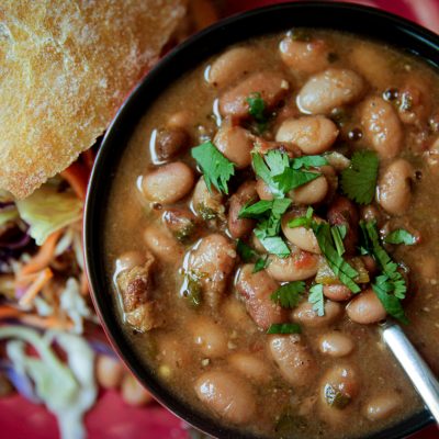 Slow Cooker Charro Beans with a cilantro garnish in a bowl with a side of bread and a salad