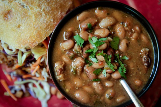 Slow Cooker Charro Beans with a cilantro garnish in a bowl with a side of bread and a salad