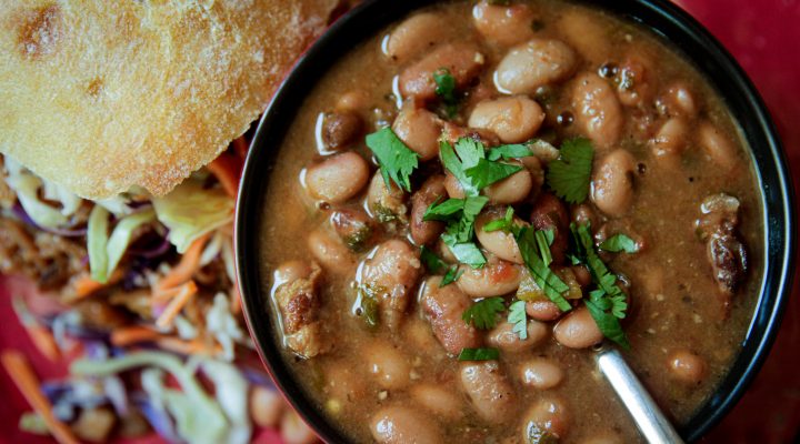 Slow Cooker Charro Beans with a cilantro garnish in a bowl with a side of bread and a salad