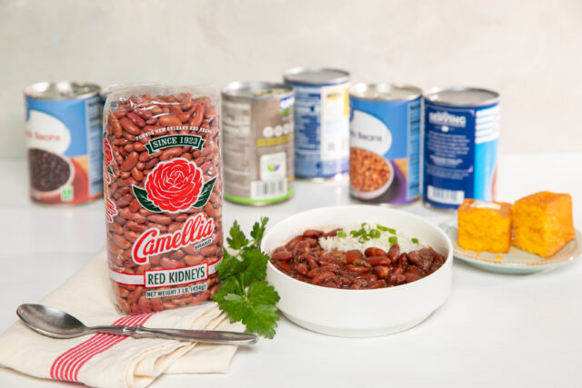bag of Camellia Brand dry red beans standing up next to a small, white, bowl of cooked red beans and rice, with other brand's can of red beans in background