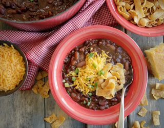 a bowl of 3 bean vegetarian chili next to frito chips, shredded cheese and a dutch oven of beans