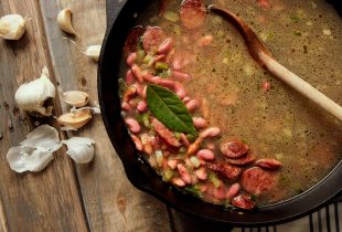 a top down view of a cast iron pot with beans, water and bay leaf added to pot