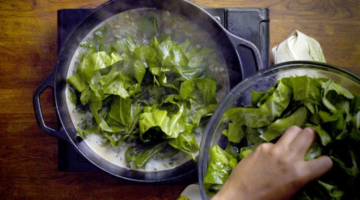 a chef adding collard greens to his pot that is cooking