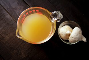 2 cups of chicken broth in a pyrex measuring cup next to a small cup of 2 whole garlic cloves