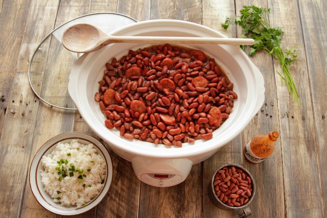 Red beans inside a slow cooker with a bowl of rice on the side