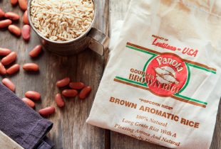 a bag of panola gourment brown rice next to a meta measuring cup of brown rice with red beans scattered on the table