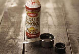 a measuring spoon of liquid smoke next to a container of it
