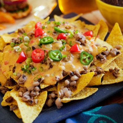 close up of black eye peas nachos inclusing tortilla chips, queso, red and green peppers and cillantro on top