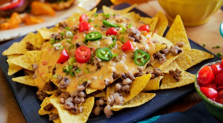 close up of black eye peas nachos inclusing tortilla chips, queso, red and green peppers and cillantro on top