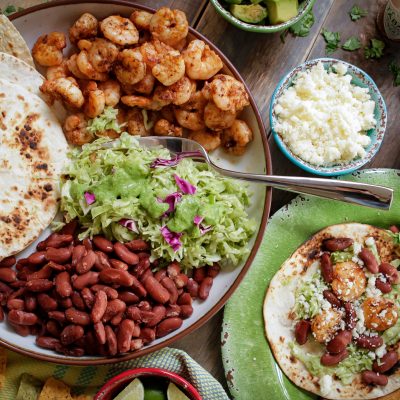 Place of tortillas, grilled shrimp, guacamole, red beans and cheese with topping on the side.