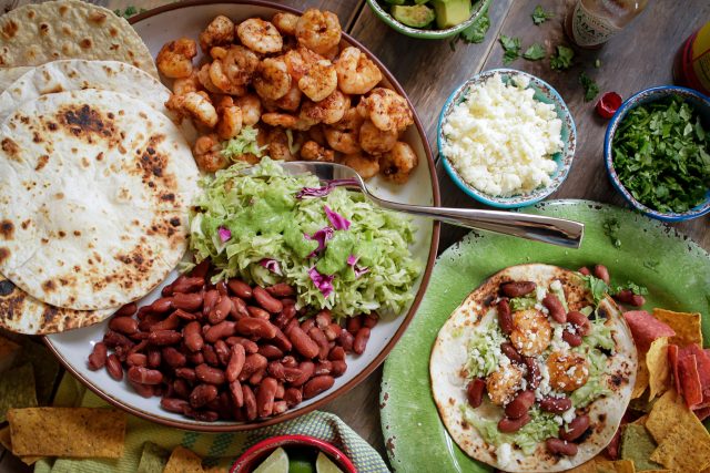 Place of tortillas, grilled shrimp, guacamole, red beans and cheese with topping on the side.