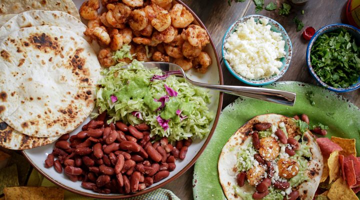 Place of tortillas, grilled shrimp, guacamole, red beans and cheese with topping on the side.