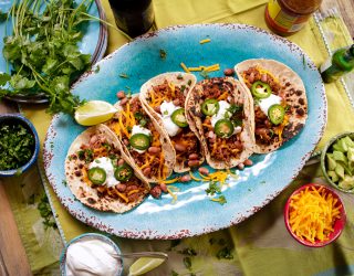 5 shredded pork and bean street tacos served on a plate with jalapenos and sour creme