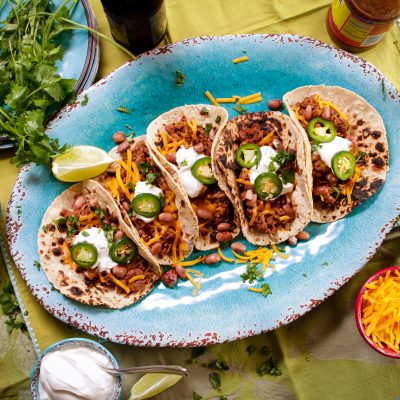 5 shredded pork and bean street tacos served on a plate with jalapenos and sour creme