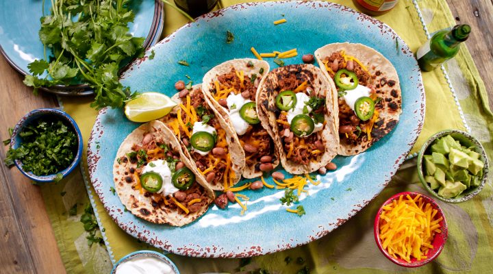 5 shredded pork and bean street tacos served on a plate with jalapenos and sour creme