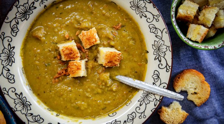 a bowl of green split pea and ham soup with croutons in it and a side of bread