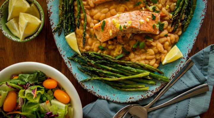 a plate of roasted salmon white beans preserved by lemons next to a small bowl of salad