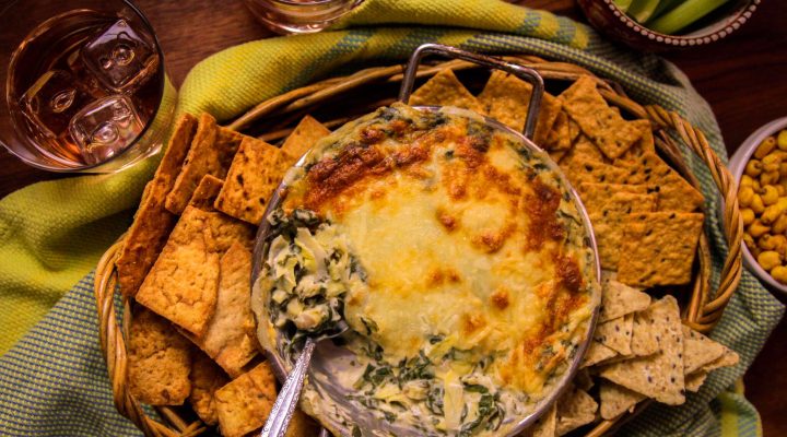 a bowl of spinach artichoke white bean dip surrounded by various bread and crackers