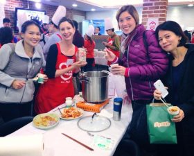 4 people crowd around a cook pot with the camellia logo in korea