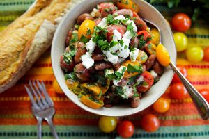 Bowl of Red Bean Red Bean & Goat Cheese Mediterranean Salad with fresh, whole cherry tomatoes, and french bread on the side