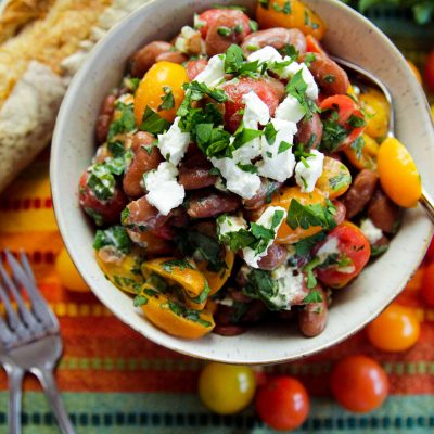 Bowl of Red Bean Red Bean & Goat Cheese Mediterranean Salad with fresh, whole cherry tomatoes, and french bread on the side