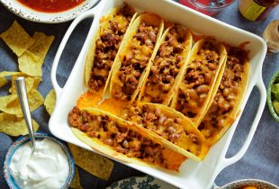 tacos and beans served in a sqaure glass plate next to sour cream and tortilla chips