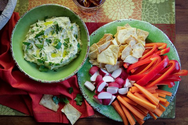 a bowl camellia bran beans hummas next to a plate of pita bread, carrots, and orange bell peppers