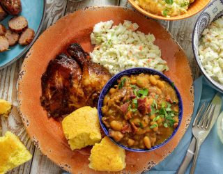 a plate of baked beans and bbq chicken with a side of coleslaw and corn bread