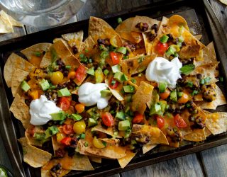 a baking pan of nachos topped with beans, sour cream, avacados and tomatos