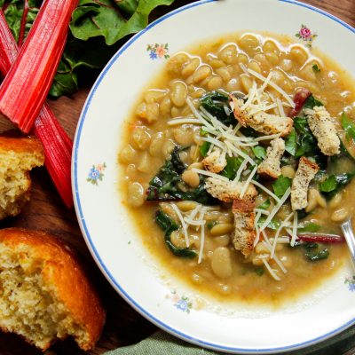 instant pot lima bean soup in a bowl with assorted greens and a side of bread