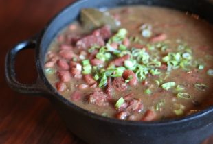 a close up of a cast iron pot full of red beans, sausage and chopped green onions