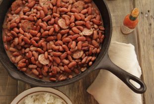 a cast iron pan full of red beans and sausage next to an open bottle of tabasco sauce