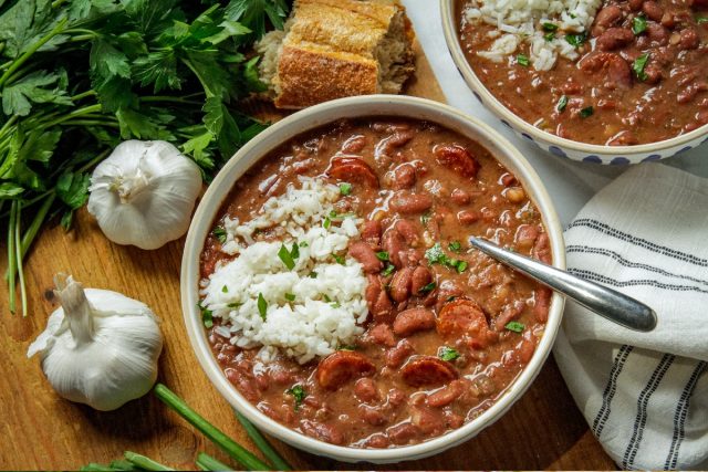 Two bowls of red beans and rice with french bread and garlic on the side