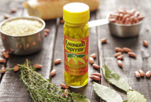 A bottle of peppered vinegar on a dark surface with scattered beans around it